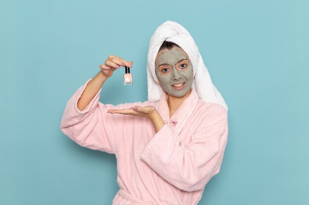 Vista frontal mujer joven en bata de baño rosa con esmalte de uñas en la pared azul limpieza belleza agua limpia ducha crema autocuidado