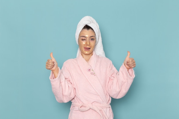 Vista frontal mujer joven en bata de baño rosa posando en la pared azul ducha limpieza belleza crema de autocuidado