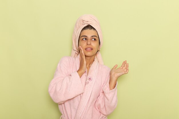 Vista frontal mujer joven en bata de baño rosa posando sobre una superficie verde