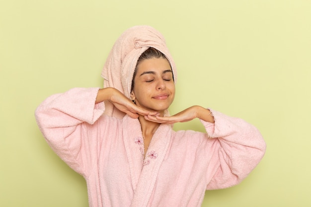 Vista frontal mujer joven en bata de baño rosa posando y sonriendo sobre superficie verde