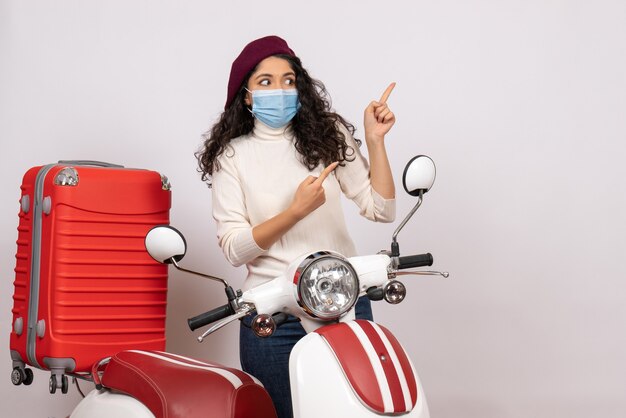 Vista frontal mujer joven con bicicleta en máscara sobre fondo blanco virus velocidad del vehículo covid- pandemia de color de motocicleta