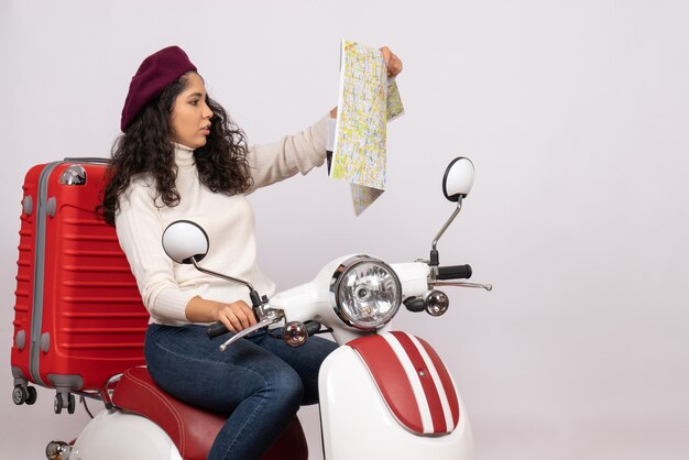 Vista frontal mujer joven en bicicleta observando mapa sobre fondo blanco ciudad color carretera vehículo de vacaciones velocidad de paseo en motocicleta