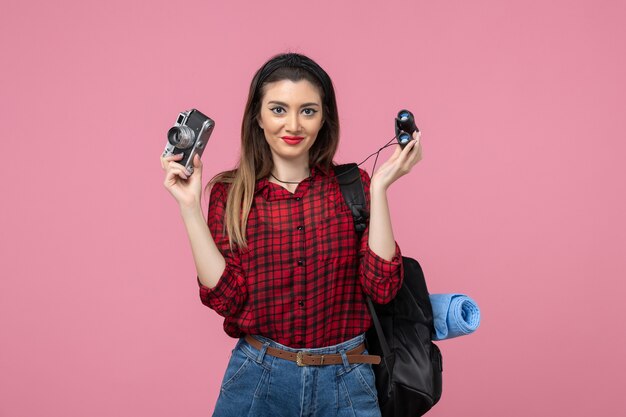 Vista frontal mujer joven con binoculares y cámara sobre fondo rosa mujer de color humano