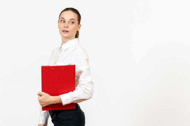 Vista frontal mujer joven en blusa blanca con archivo rojo en sus manos sobre fondo blanco trabajo de oficina emoción femenina modelo de sentimiento