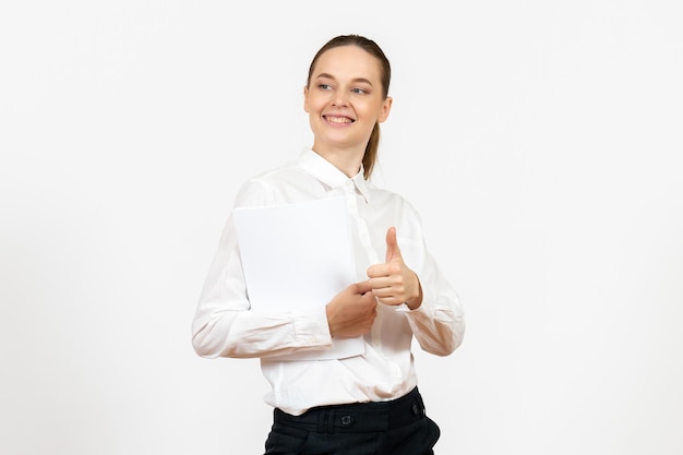 Vista frontal mujer joven en blusa blanca sosteniendo diferentes documentos y sonriendo sobre fondo blanco emoción femenina sentimiento trabajo de oficina