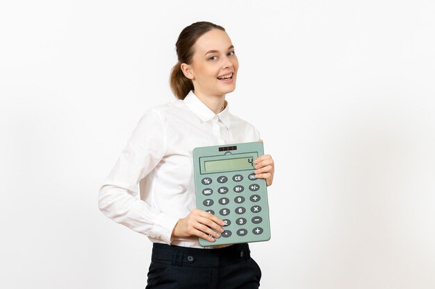 Vista frontal mujer joven en blusa blanca sosteniendo enorme calculadora sobre fondo blanco oficina emoción femenina sentimiento trabajo trabajador blanco