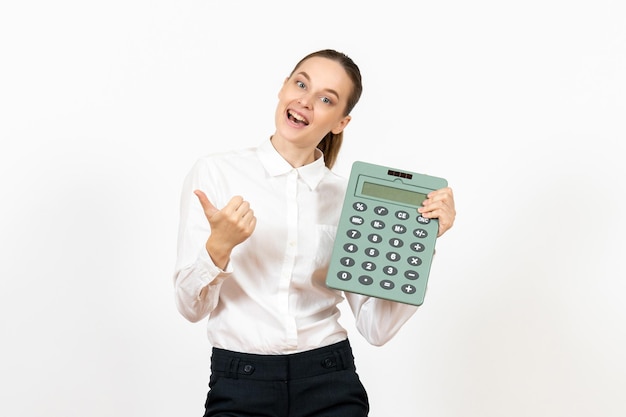 Vista frontal mujer joven en blusa blanca sosteniendo enorme calculadora sobre fondo blanco oficina emoción femenina sentimiento trabajo