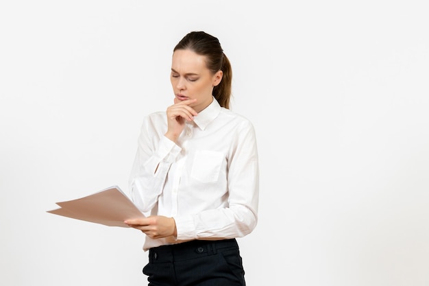 Vista frontal mujer joven en blusa blanca sosteniendo y leyendo documentos sobre fondo blanco oficina de sentimiento de emoción de trabajo femenino