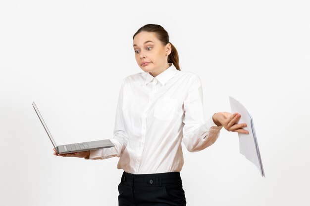 Vista frontal mujer joven en blusa blanca sosteniendo portátil y documentos sobre un fondo blanco claro modelo de sentimiento de emoción de oficina de trabajo femenino