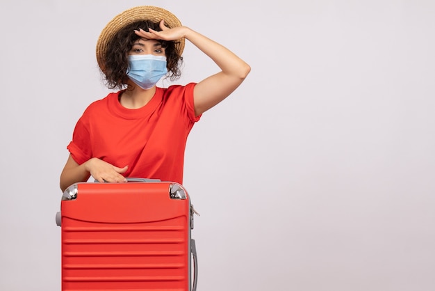 Vista frontal mujer joven con bolsa en máscara mirando a distancia sobre fondo blanco color covid- viaje vacaciones turísticas pandemia viaje virus del sol