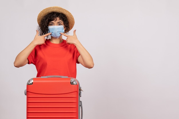 Foto gratuita vista frontal mujer joven con bolsa en máscara sobre fondo blanco virus covid- viaje de color de vacaciones de sol turístico