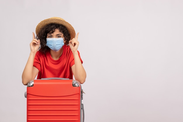 Vista frontal mujer joven con bolsa roja en máscara sobre fondo blanco color sol covid pandemia viaje turístico virus