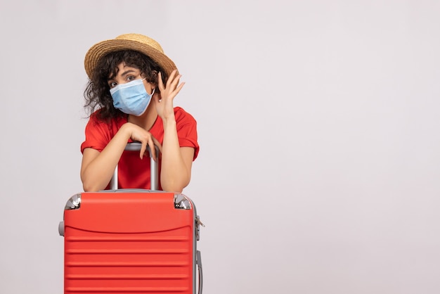 Vista frontal mujer joven con bolsa roja en máscara sobre fondo blanco color sol covid pandemia viaje turístico virus