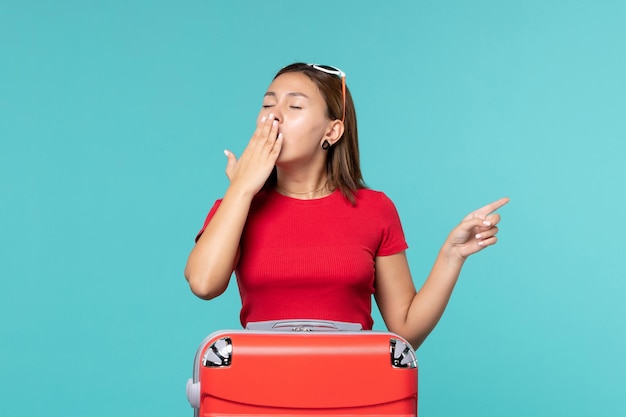 Vista frontal mujer joven con bolsa roja preparándose para vacaciones bostezando en el espacio azul