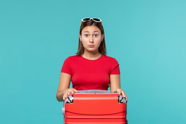 Vista frontal mujer joven con bolsa roja preparándose para las vacaciones con expresión de sorpresa en el espacio azul