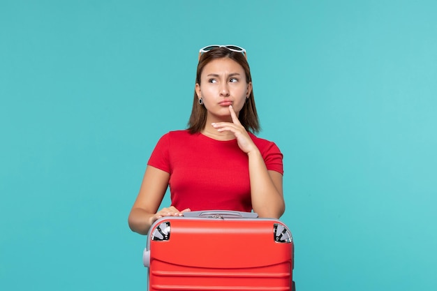 Vista frontal mujer joven con bolsa roja preparándose para las vacaciones y pensando en el espacio azul