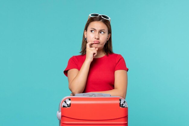 Vista frontal mujer joven con bolsa roja preparándose para las vacaciones y pensando en el espacio azul