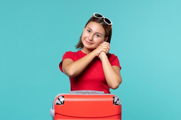 Vista frontal mujer joven con bolsa roja preparándose para las vacaciones y sonrisa en el espacio azul