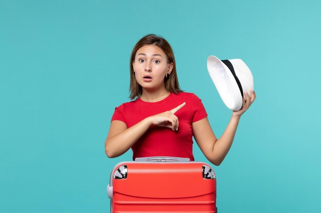 Vista frontal mujer joven con bolsa roja sosteniendo su sombrero en el espacio azul