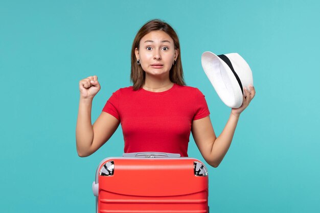 Vista frontal mujer joven con bolsa roja sosteniendo su sombrero en el espacio azul