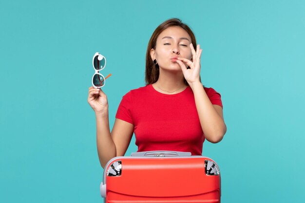 Vista frontal mujer joven con bolsa roja sosteniendo sus gafas de sol en el espacio azul claro