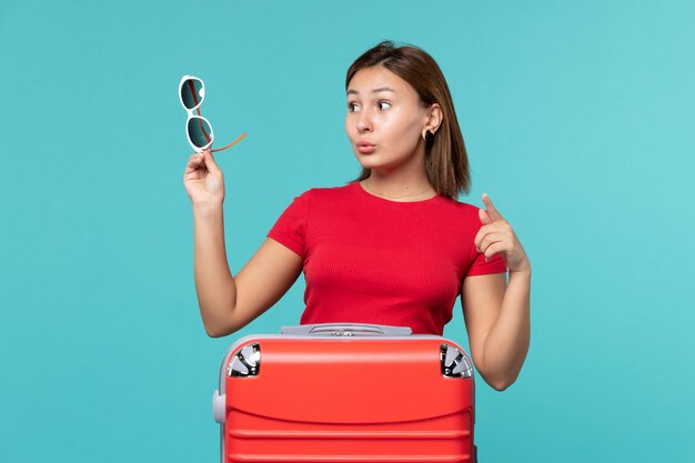 Vista frontal mujer joven con bolsa roja sosteniendo sus gafas de sol en el espacio azul