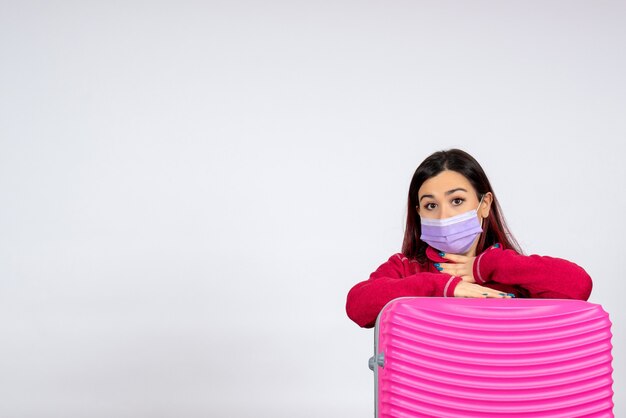 Vista frontal mujer joven con bolsa rosa en máscara estéril en la pared blanca color virus vacaciones covid pandemia viaje mujer