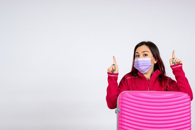 Vista frontal mujer joven con bolsa rosa en máscara estéril en una pared blanca viaje vacaciones color covid- mujer pandemia de virus