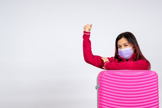 Vista frontal mujer joven con bolsa rosa en máscara flexionando sobre pared blanca