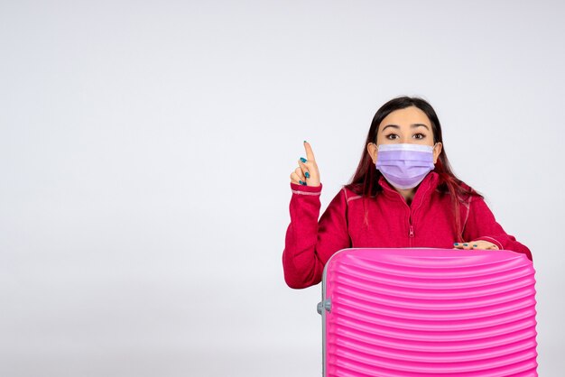 Vista frontal mujer joven con bolsa rosa en máscara en la pared blanca mujer virus covid- pandemia de viaje de color