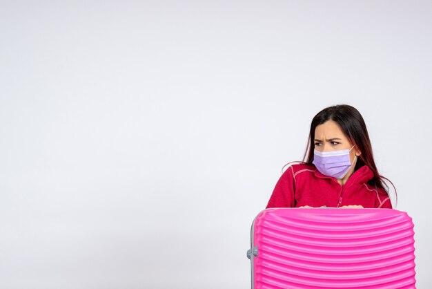 Vista frontal mujer joven con bolsa rosa en máscara en la pared blanca mujer virus pandémico vacaciones covid- viaje de color