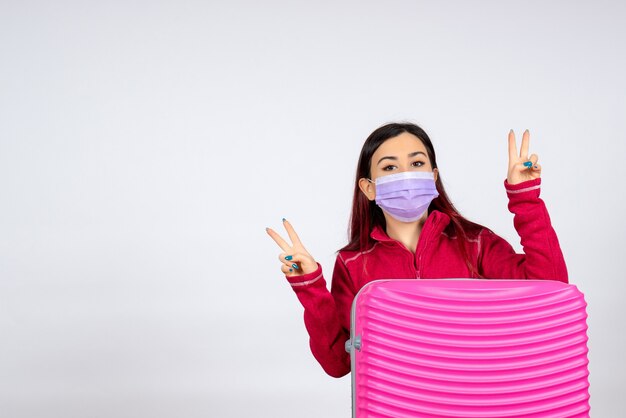 Vista frontal mujer joven con bolsa rosa en máscara en la pared blanca mujer de virus vacaciones viaje de color covid