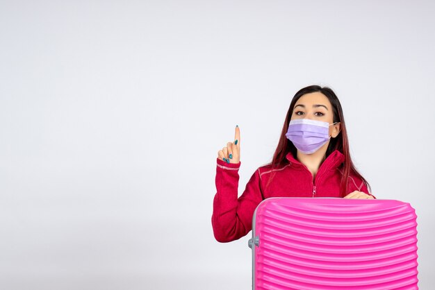 Vista frontal mujer joven con bolsa rosa en máscara en la pared blanca mujer de virus vacaciones viaje pandémico de color covid