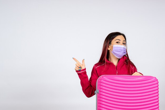 Vista frontal mujer joven con bolsa rosa en máscara sobre el virus de escritorio blanco mujer vacaciones color covid viaje pandémico