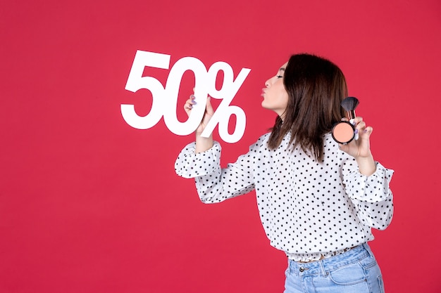 Foto gratuita vista frontal mujer joven con borla en polvo para maquillaje y pared roja