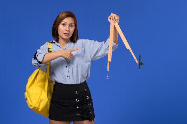 Vista frontal de la mujer joven en camisa azul con figura de madera en la pared azul