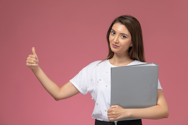 Vista frontal mujer joven en camisa blanca con archivo gris en la pared rosa, modelo mujer pose mujer