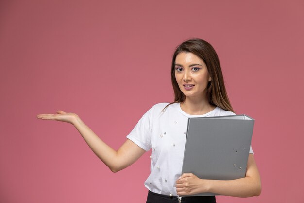 Vista frontal mujer joven en camisa blanca con archivo gris en pared rosa, mujer modelo