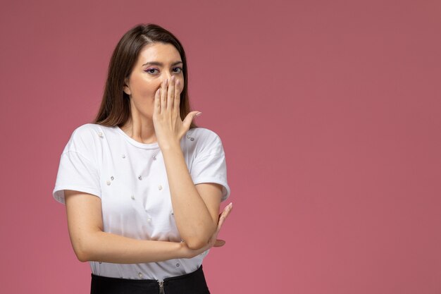 Vista frontal mujer joven con camisa blanca bostezando en la pared de color rosa claro, pose de mujer modelo de mujer