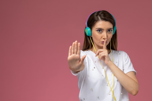 Foto gratuita vista frontal mujer joven en camisa blanca escuchando música a través de sus auriculares de colores en la pared rosa, modelo de mujer de color posando mujer