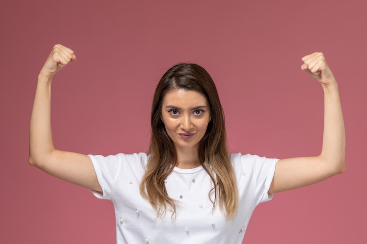 Foto gratuito vista frontal mujer joven en camisa blanca flexionando en pared rosa