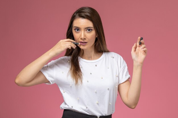 Vista frontal mujer joven en camisa blanca con lápiz de maquillaje en la pared rosa, modelo de mujer de color posando mujer