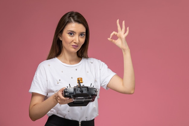 Foto gratuita vista frontal mujer joven en camisa blanca con mando a distancia en la pared rosa, modelo de mujer de color