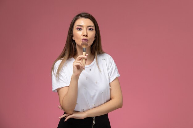 Vista frontal mujer joven en camisa blanca con pincel para maquillaje en la pared rosa color mujer modelo posando mujer