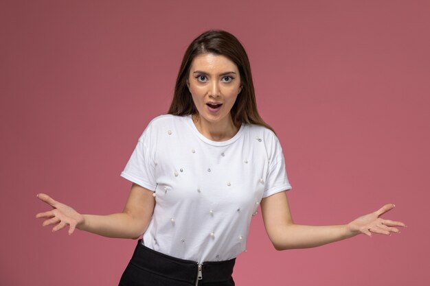 Vista frontal mujer joven con camisa blanca posando de manera emocional en la pared rosa, modelo de pose de mujer de color