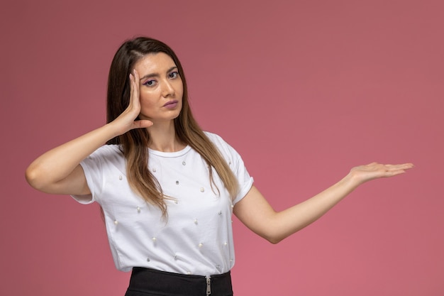 Vista frontal mujer joven en camisa blanca posando con la mano levantada en la pared rosa, modelo de mujer de color posando mujer