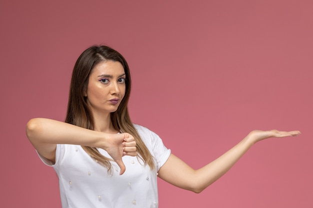 Foto gratuita vista frontal mujer joven con camisa blanca posando mostrando signo diferente en la pared rosa, mujer de color pose modelo mujer