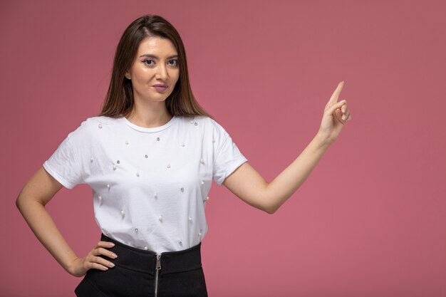 Vista frontal mujer joven en camisa blanca posando con una sonrisa en la pared rosa, modelo de pose de mujer de color de foto