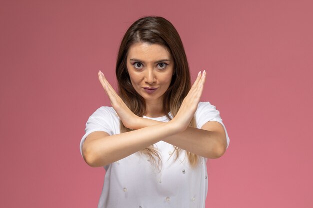 Vista frontal mujer joven en camisa blanca que muestra el signo de prohibición en la pared rosa, mujer de color modelo mujer