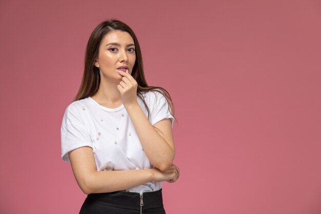 Vista frontal mujer joven en camisa blanca simplemente posando en la pared rosa, modelo de mujer de color posando mujer